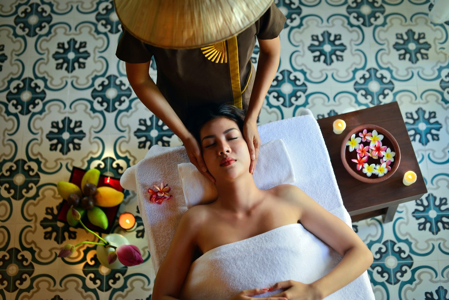 A woman receives a relaxing head massage at a luxury spa with traditional patterned tiles and flowers.
