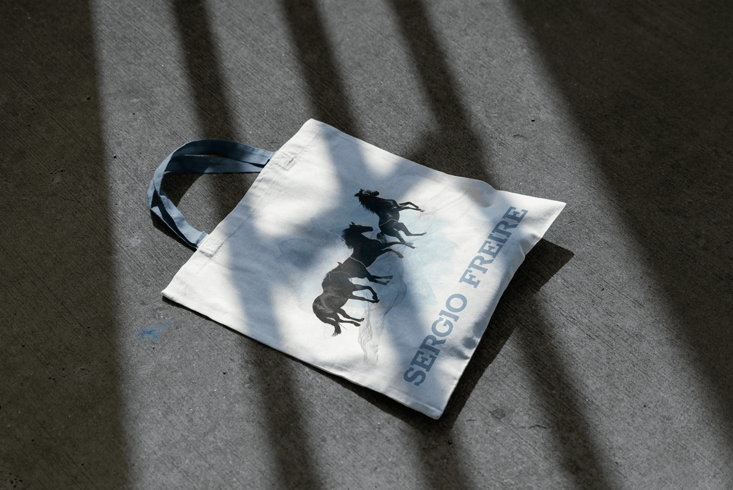 Totebag en el suelo con un diseño de caballos y el logo de Sergio Freire en azul