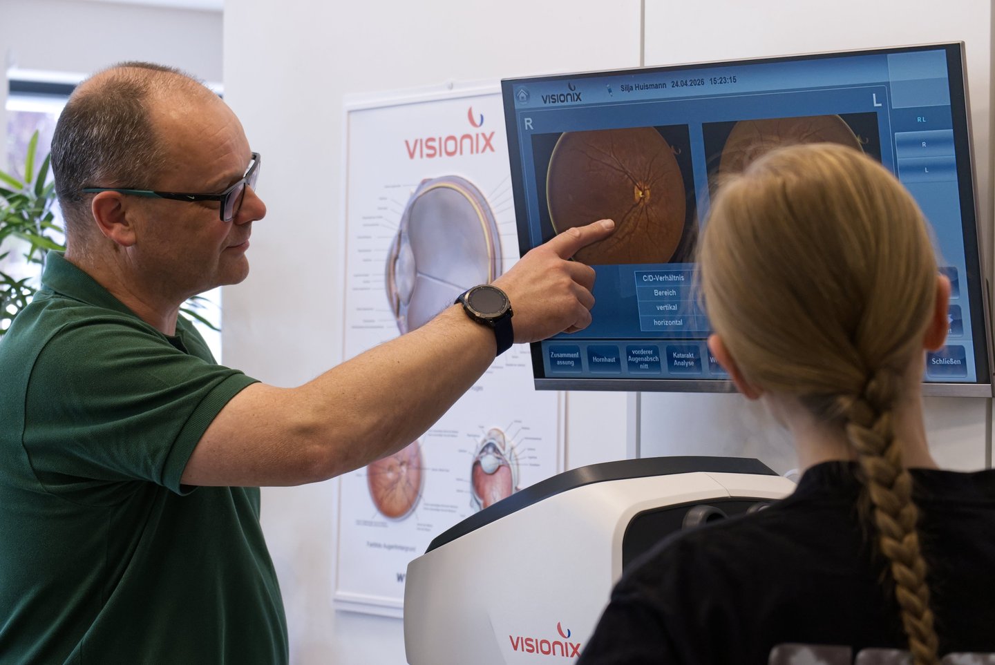 Optometrist pointing to retinal scan results on a Visionix monitor during an eye exam.