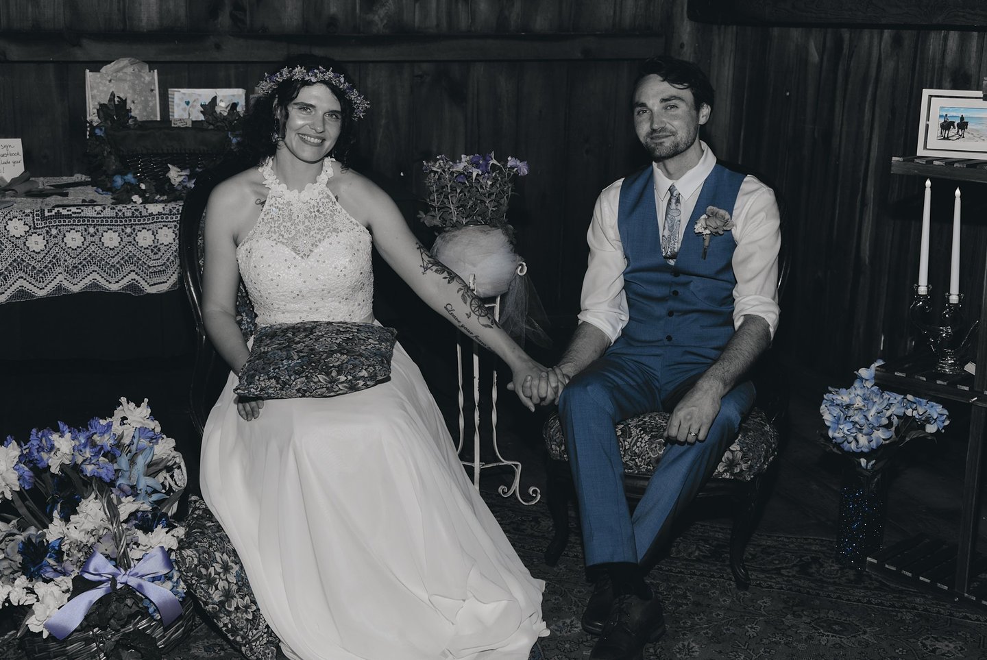 a bride in a white dress and a groom in a blue suit holding hands and sitting in a decorated barn