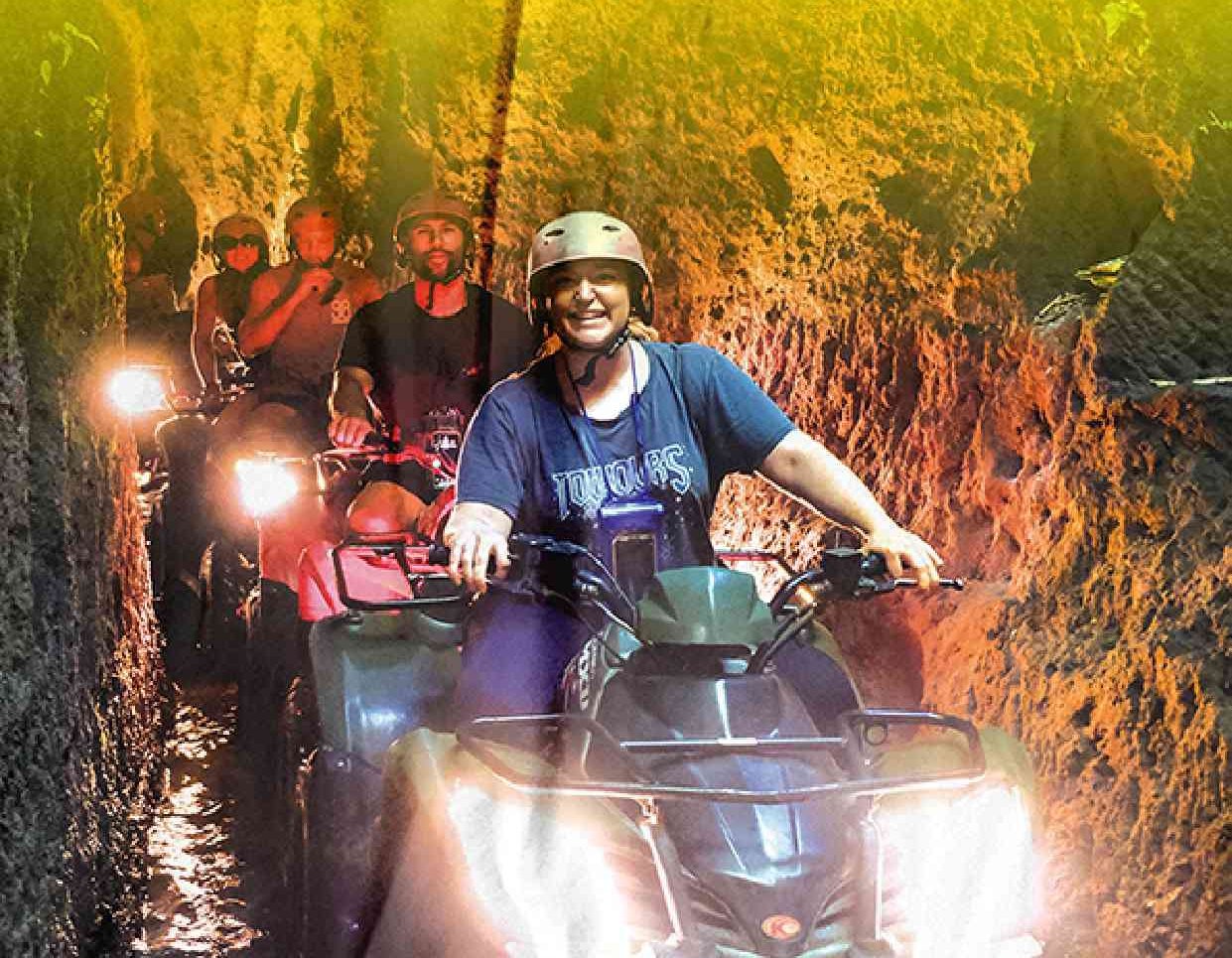 Tourists riding Kuber ATV quad bikes through a dark underground cave tunnel for an adventure tour.