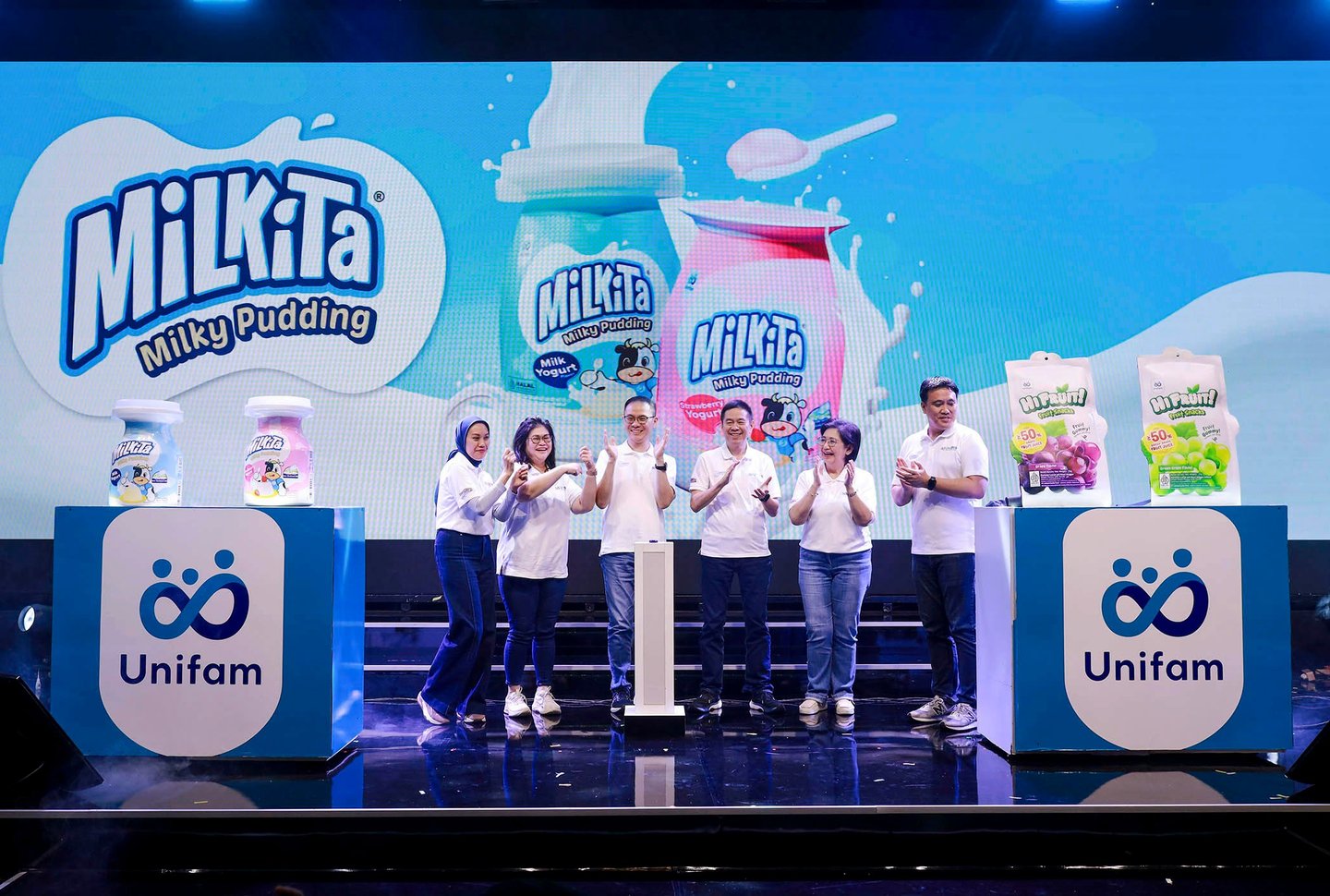 Unifam team launching Milkita Milky Pudding products on stage with digital background and banners.