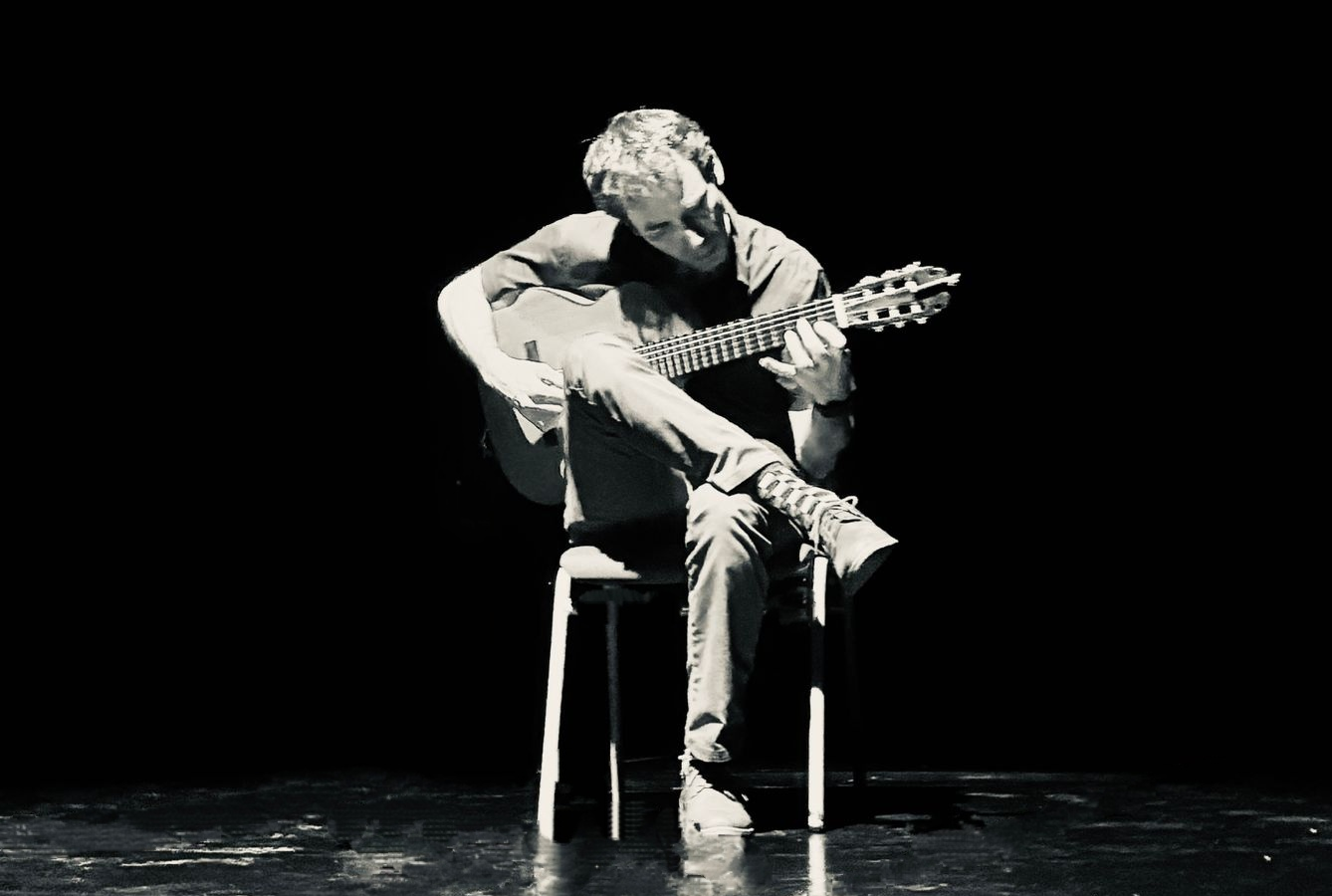Paco playing the guitar under a theatrical overhead light.