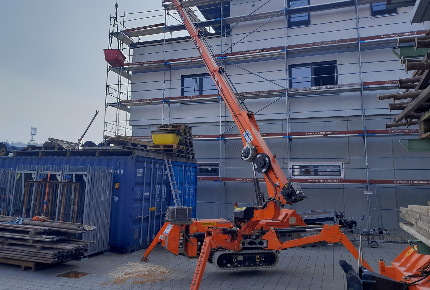 Oranger Kran "Jekko SPD360" auf Baustelle vor eingerüstetem Mehrfamilienhaus.