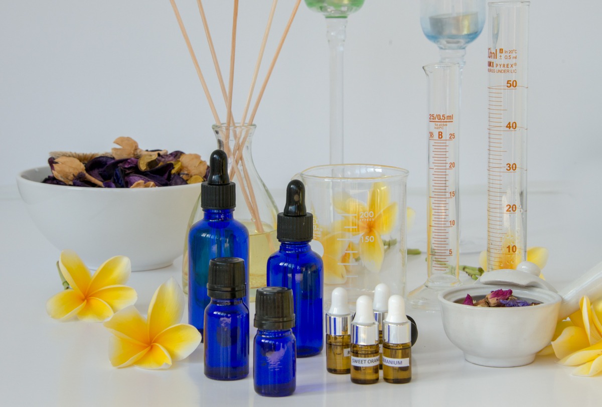 Blue glass apothecary bottles with essential oils, frangipani flowers, and laboratory glassware for aromatherapy.