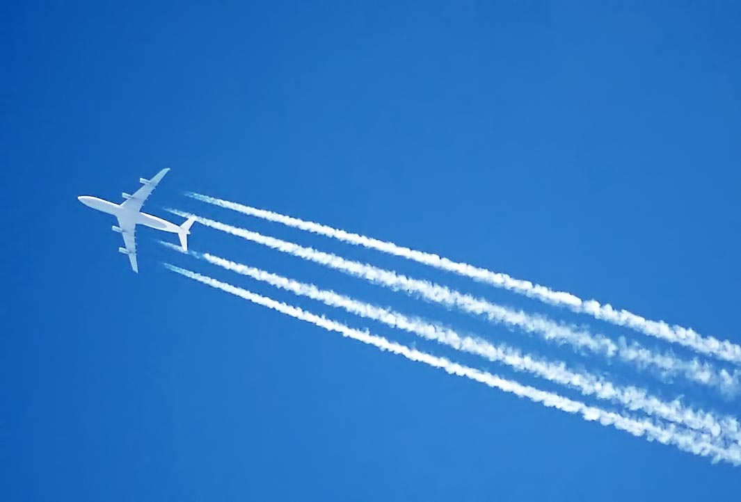 White passenger jet airplane flying through a clear blue sky leaving long white vapor contrails.