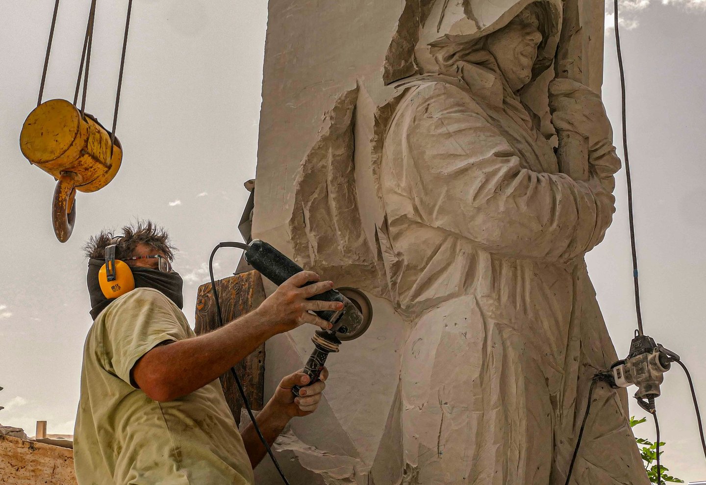 Professional sculptor using an angle grinder to carve a detailed stone statue outdoors.