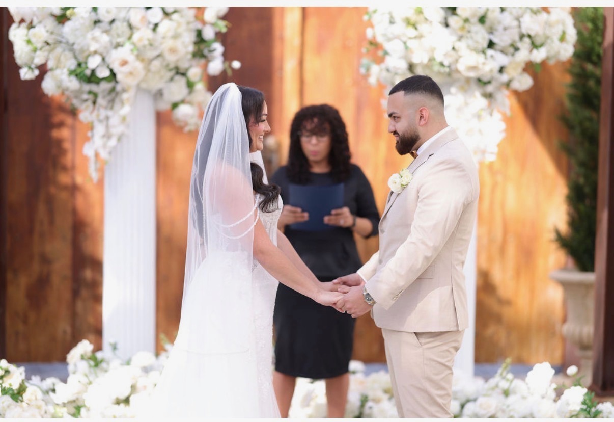 Bride and groom holding hands during an outdoor wedding ceremony with white floral arrangements.