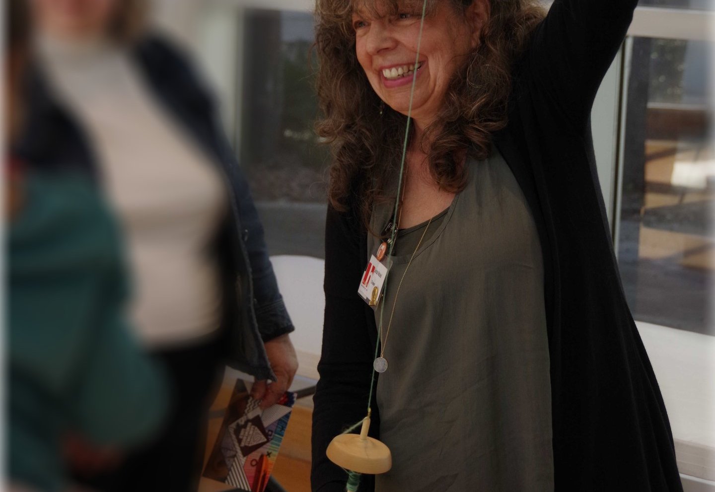 Photo of Linda Nickel demonstrating spinning yarn with a drop spindle.