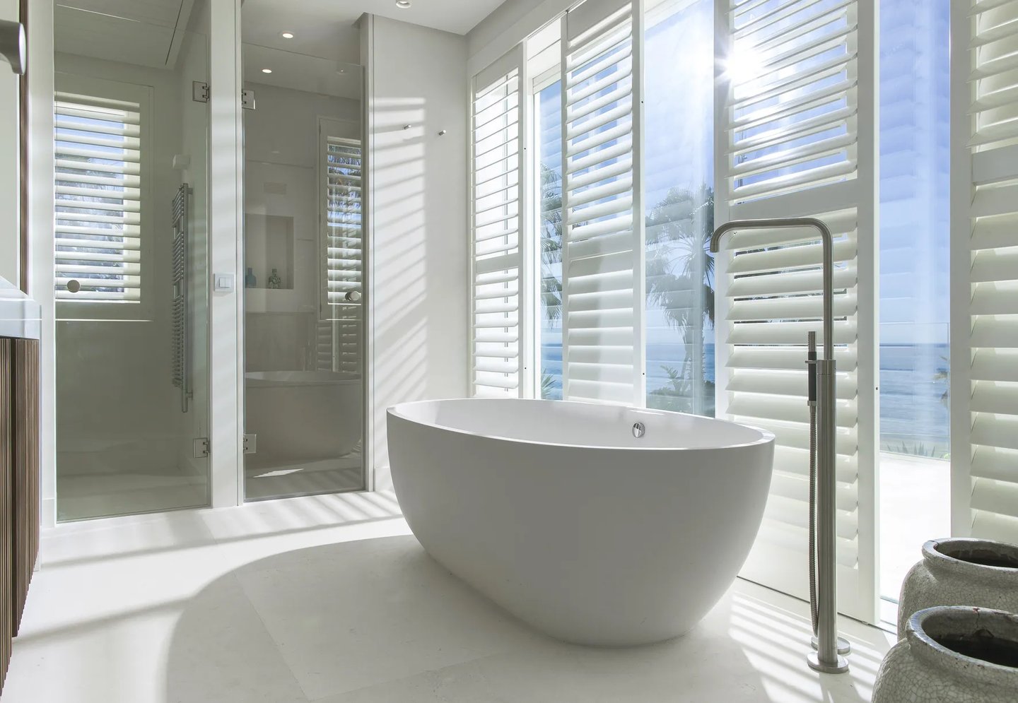Freestanding bathtub with ocean views and shuttered windows