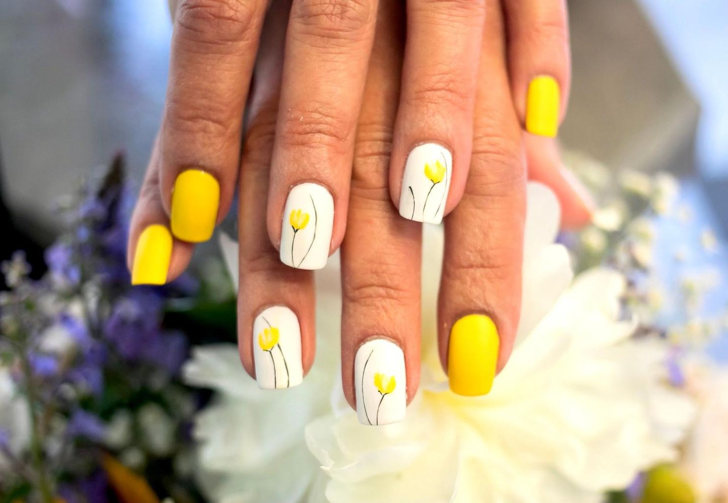 Yellow and white spring manicure with hand-painted floral nail art on white accent nails.