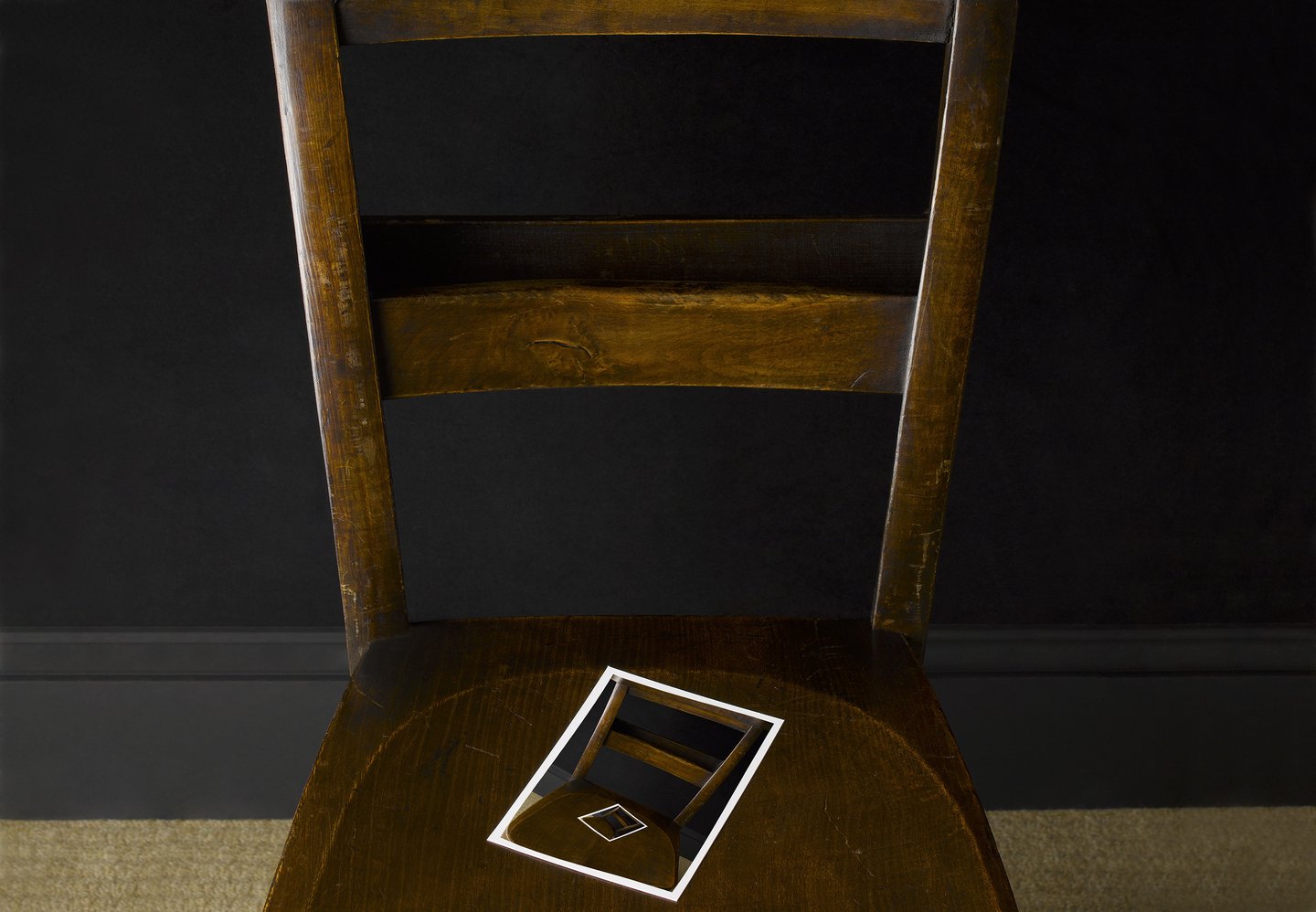brown wooden chair against a black wall with photo of chair on its seat