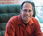 a man in a red shirt and jeans sitting in a chair