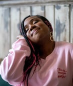 A Black woman with long pink and black hair and a pink jumper with red writing