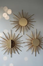 Set of three gold sunburst mirrors on a light grey wall.