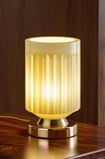 Soft yellow glass table lamp with a gold base, lit warmly against wood.