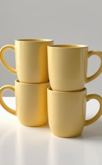 Set of four stackable butter yellow mugs with rounded handles.