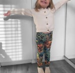 a little girl standing in a room with her arms outstretched out wearing peacock print leggings