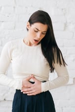 Mulher com a mão no estômago indicando dor abdominal e prisão de ventre