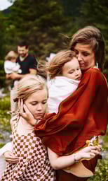 a woman in a red dress is holding her children with wind in their hair. Dad holds daughter in back.