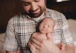 Dad holding newborn son against his chest, looking down at him.