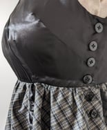 The side button closure of a black/gold plaid and black satin flowy cocktail dress