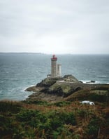 a lighthouse on a rocky island with a car parked on the side of the road
