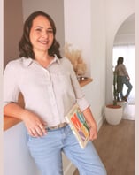 Milly leaning on a counter, holding a book about money management, in a well-decorated home