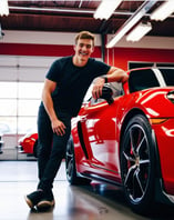 a young man smiles happily next to his sports car after receiving top-notch service at AMI Service