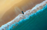 a person standing on a beach with a surfboard. arbab naimat kasi balochistan gawadar