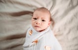 Newborn wrapped in a white swaddle with gold hearts, looking directly at the camera during a Hibbing