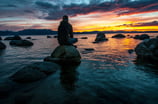 a man sitting on a rock in the water watching the sunrise