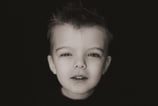 4-year-old boy squints curiously into the camera during a personality portrait session on a black ba