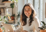Mujer joven sonríe frente a su laptop en un espacio luminoso, representa emprendimientos digital en un ambiente inspirador.