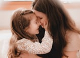 Mother and daughter share a tender moment with foreheads touching and eyes closed, as the little gir