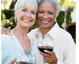 two lovely older women smiling and holding glasses of red wine