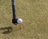 A golf club with a 'TeeZUP' attachment holding an orange tee and a golf ball, set up on a grassy course, ready for a shot