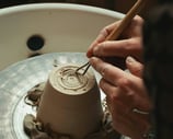 a person is making a clay potted with a wooden spoon