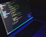 A laptop displaying colored code lines on a dark-themed text editor screen.