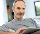 a man sitting on a couch with a tablet computer Martin PE / COACH