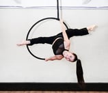 Vrouw in zwarte outfit voert een aerial hoop oefening uit bij De Polecats Fabriek in Gent