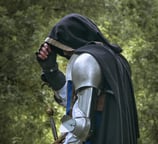 Homme mystérieux en armure et cape sur un fond de feuilles verdoyante. C'est peut-être un rôdeur