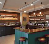 An indoor space under renovation, featuring a bar counter with various construction materials and tools scattered around. The walls are decorated with floral wallpaper. Multiple pendant lights hang from the ceiling, casting a warm glow. A ladder and several cardboard boxes are visible in the background.