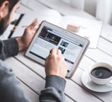 Man using a tablet to read digital news at a desk with a cup of coffee