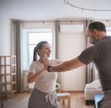 Pareja adulta sonriendo y haciendo un ejercicio de baile en su sala de estar, participa