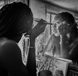 Photo artistique noire et blanc d'une jeune femme noire qui se requi se remaquille dans le miroir d'un intérieur haussmannien