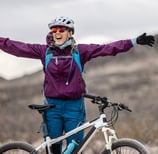 a young woman standing in front of her mountain bike with her arms outstretched
