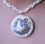 A string of pearls with a pendant made of clay. Pendant includes a  hand-drawn landscape in ink.
