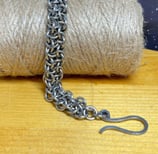 Photo of a chainmaille bracelet made of stainless steel draped over a bundle of jute twine