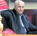 a man in a black jacket and tie dye on a chair
